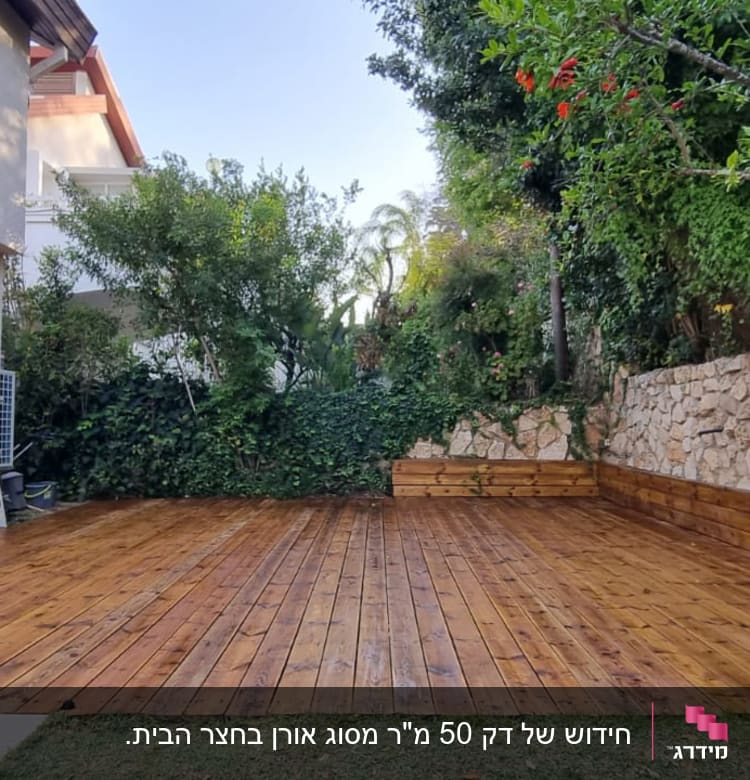 דק עץ בגינה עם קיר אבן וצמחייה ירוקה